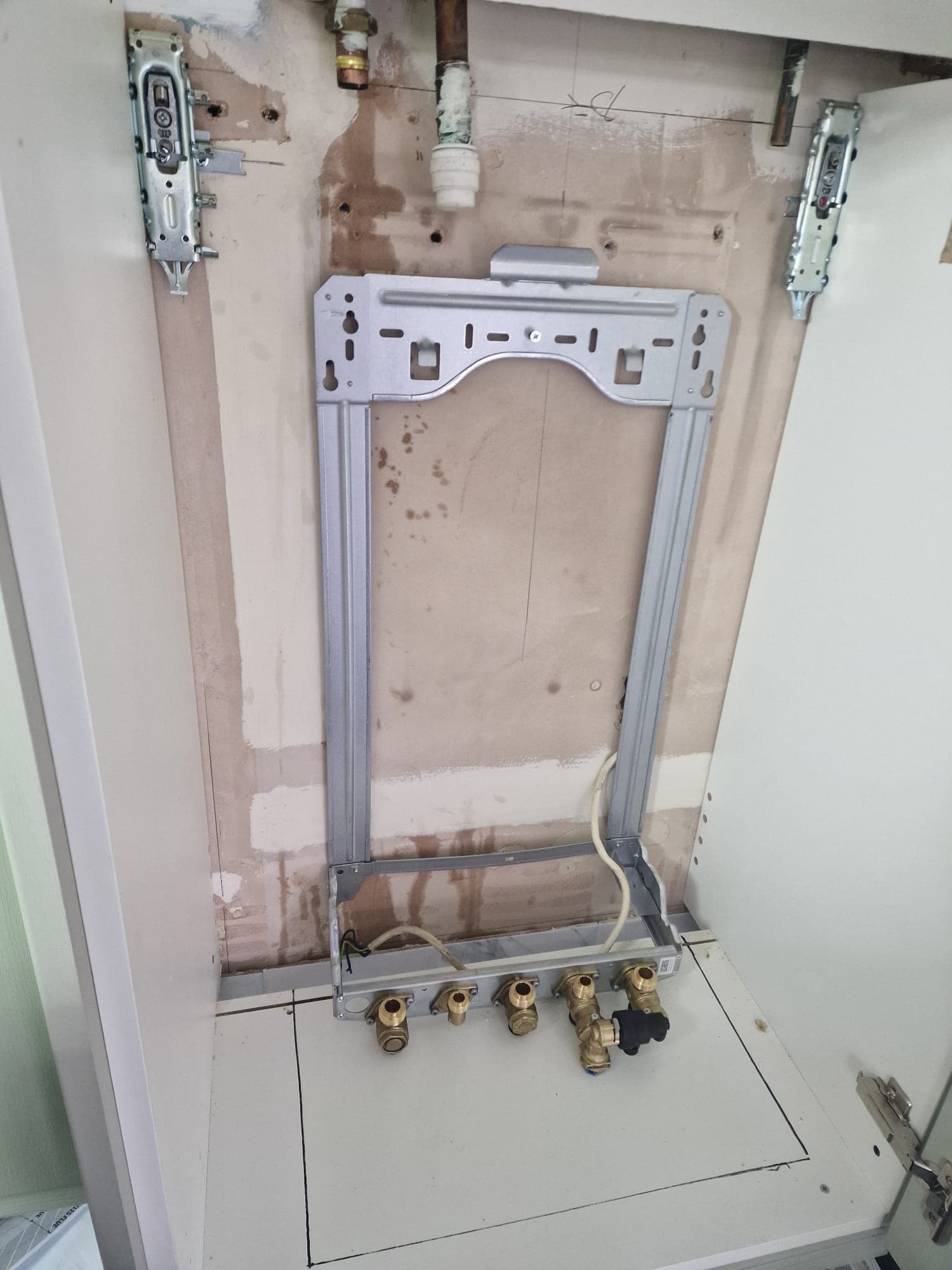 Boiler mounting frame and isolating valves fitted in kitchen cabinet before boiler installation